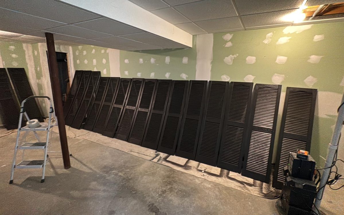 Row of window shutters freshly painted black, drying on drop cloths