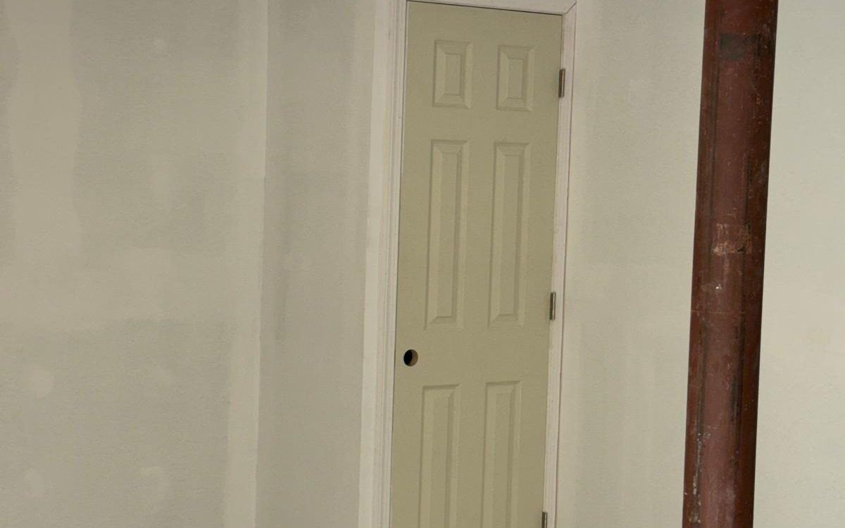 Finished basement with smooth white walls, painted trim and a paneled door