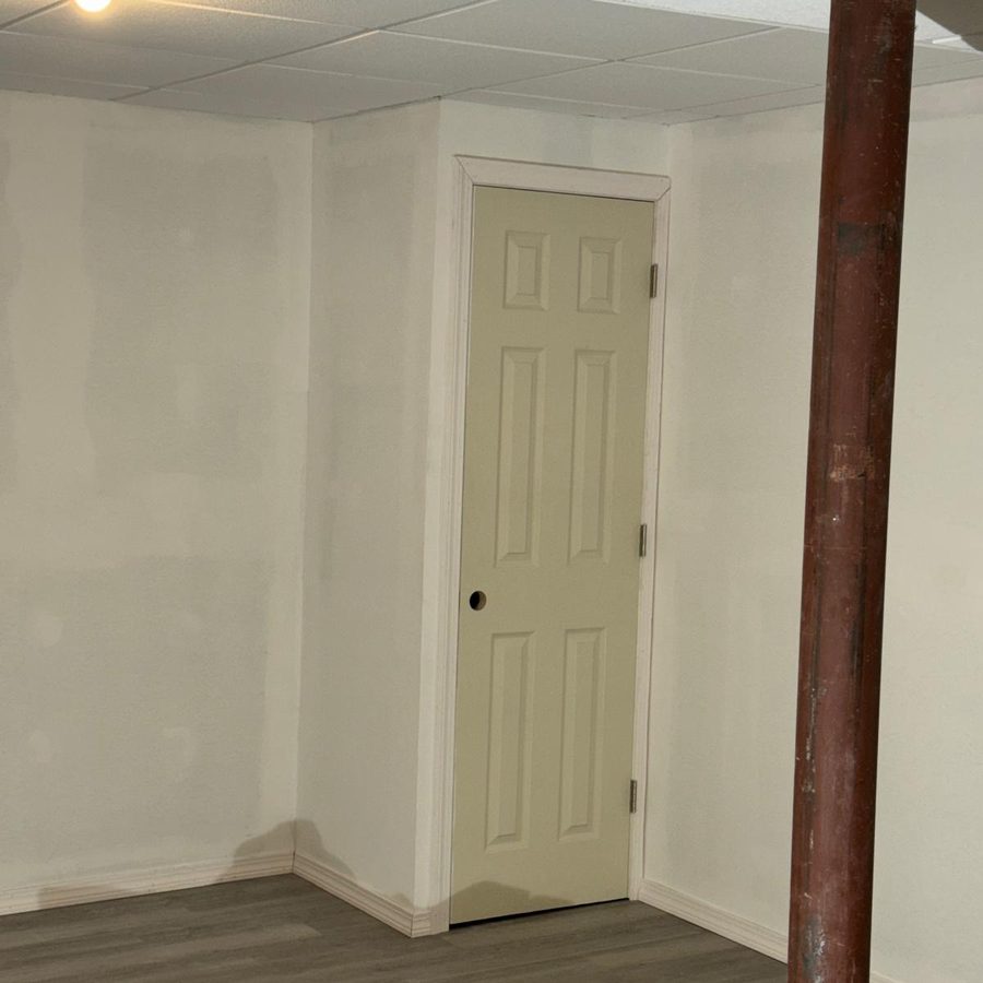 Finished basement with smooth white walls, painted trim and a paneled door