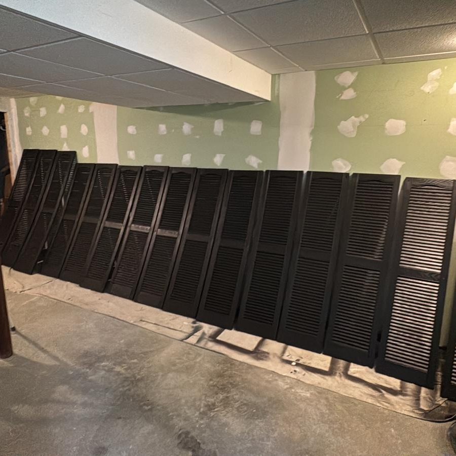 Row of window shutters freshly painted black, drying on drop cloths