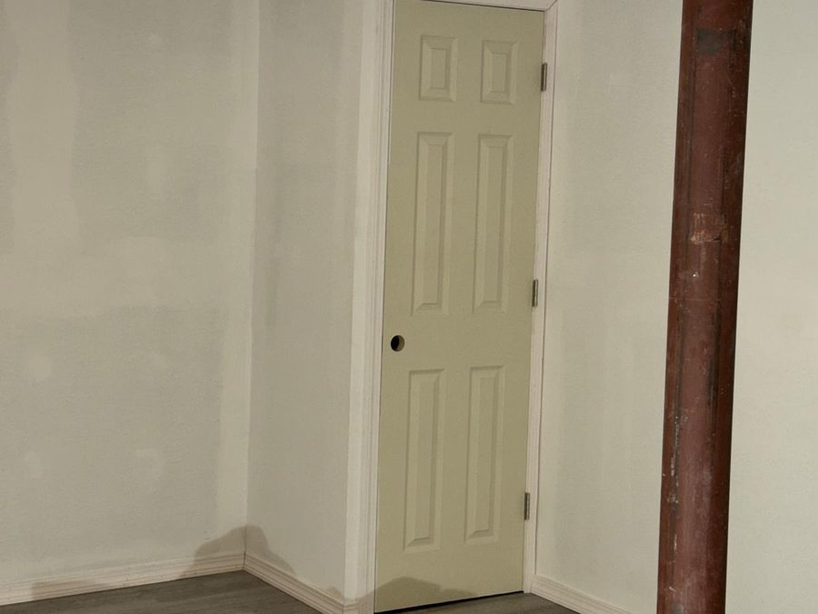 Finished basement with smooth white walls, painted trim and a paneled door