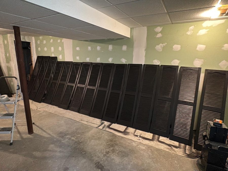 Row of window shutters freshly painted black, drying on drop cloths