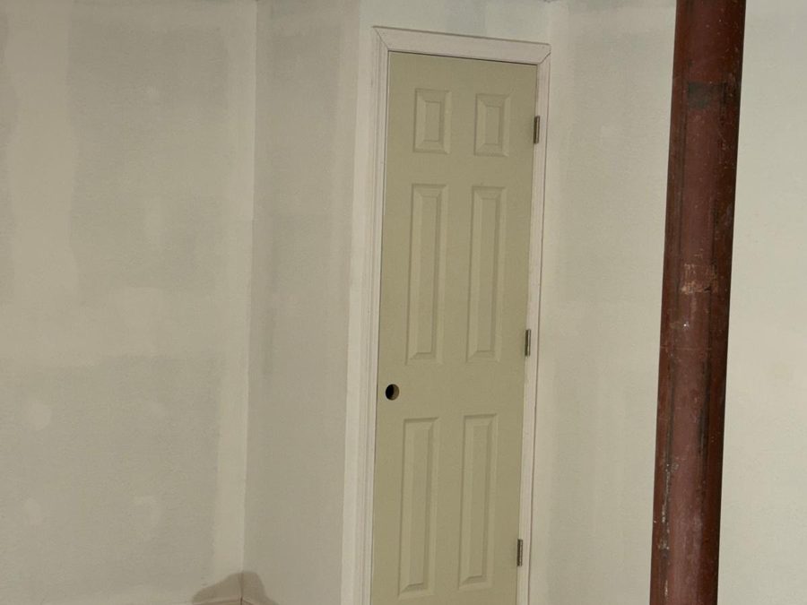 Finished basement with smooth white walls, painted trim and a paneled door