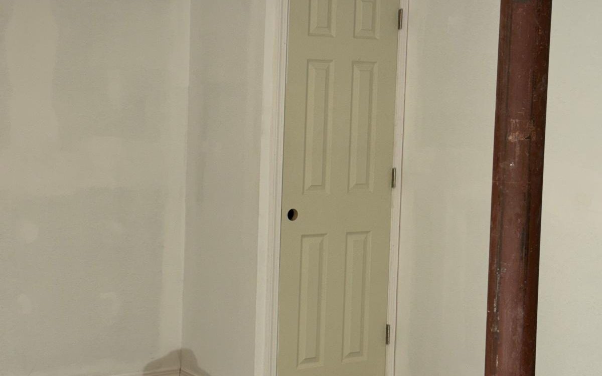 Finished basement with smooth white walls, painted trim and a paneled door